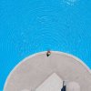 Una persona seduta sul bordo di una piscina circolare con increspature concentriche sull'acqua blu.