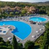 Due piscine di forma irregolare in un resort con ombrelloni, circondate da alberi e colline.