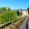 Un ponte in legno conduce a una villa in pietra tra alberi verdi.
