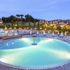 Piscina circolare illuminata di sera, circondata da sdraio e ombrelloni, con villette sullo sfondo.