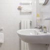 Bagno con lavabo bianco, specchio, asciugamani e accessori su pareti piastrellate di bianco.