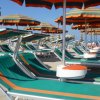 Lettini verdi sotto ombrelloni color arancio e verde su una spiaggia soleggiata.