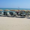 Spiaggia con lettini e ombrelloni arancioni e verdi di fronte al mare calmo.