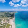 Spiaggia con mare turchese e case lungo la costa.