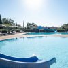 Piscina rotonda con scivolo blu e ombrelloni attorno, illuminata dal sole.