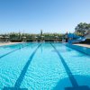 Piscina rettangolare con corsie, scivolo blu e lettini sotto ombrelloni.