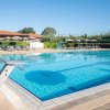Piscina con trampolini, ombrelloni grigi e struttura con tetto rosso sullo sfondo.