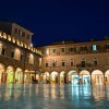 Piazza illuminata di notte con edifici storici.