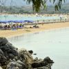 Spiaggia sabbiosa con ombrelloni blu e rocce.