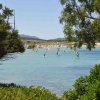 Windsurfisti su acqua calma incorniciati da alberi.