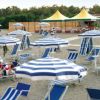 Spiaggia con ombrelloni e lettini a righe blu e bianche, persone rilassate al sole.