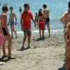 Gruppo di ragazzi in costume da bagno sulla spiaggia, alcuni in acqua, altri sulla sabbia.
