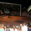 Un palco all'aperto con ballerini e pubblico attorno di sera.