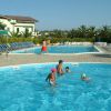 Una piscina all'aperto con bambini che nuotano e una fila di sdraio blu. Palme in lontananza.