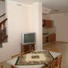 Una stanza con tavolo, televisore, scala in legno e cucina sullo sfondo.