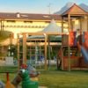 Un parco giochi con scivolo e giostra, edifici e montagne sullo sfondo.
