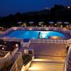 Piscina illuminata di notte, circondata da recinzione bianca e sdraio con ombrelloni.