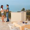 Due persone si parlano su una terrazza con vista mare, vicino a un tavolo apparecchiato.