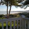 Vista di una spiaggia e del mare da un balcone con balaustra bianca, circondato da alberi.