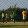 Ragazzi giocano a calcetto su prato sintetico, visti attraverso una rete.