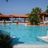 Piscina con sdraio, ombrelloni e persone che nuotano. Vegetazione verde intorno.