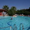 Piscina all'aperto con persone che nuotano e alberi sullo sfondo.