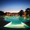 Piscina illuminata con scala e luci subacquee, circondata da piante e palme al crepuscolo.
