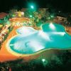 Piscina illuminata di notte con luci verdi, circondata da tavoli e vegetazione.