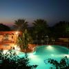 Piscina serale con palme e un cielo al tramonto sullo sfondo.