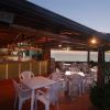 Una terrazza con tavoli e sedie di plastica bianche accanto a un bar con vista sul mare al tramonto.