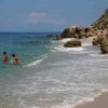 Spiaggia sabbiosa con persone in acqua e grandi rocce sulla riva.