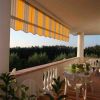 Una terrazza con tavolo bianco e sedie di plastica. Tenda da sole a righe gialle e arancioni.