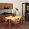 Cucina con tavolo a tovaglia gialla, quattro sedie in legno e angolo cottura con armadietti marroni.