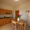 Cucina semplice, tavolo con fiori, mobili in legno chiaro, frigorifero bianco.