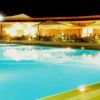 Piscina illuminata di notte con tavoli e ombrelloni, atmosfera calda e accogliente.
