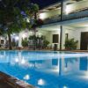 Piscina illuminata di notte con sedie a sdraio, alberi e un edificio.