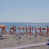 Spiaggia con ombrelloni arancioni e rosa, vista mare e una torretta di legno a sinistra.