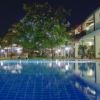 Piscina illuminata di notte, circondata da edifici e piante.