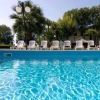 Piscina azzurra circondata da lettini bianchi e alberi.