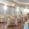 Sala da pranzo luminosa con tavoli apparecchiati, sedie di legno e tende bianche alle finestre.