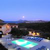 Piscina illuminata al tramonto con vista sul mare e colline in lontananza.