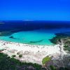 Una spiaggia con sabbia bianca e mare azzurro, circondata da una vegetazione verde.