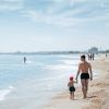 Uomo e bambino camminano su una spiaggia, aquilone verde nel cielo.