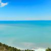 Panorama di una costa con mare turchese e cielo blu, vegetazione in primo piano.