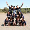 Un gruppo di persone forma una piramide umana sulla spiaggia, tutti indossano magliette blu.