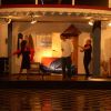 Tre persone recitano su un palco con arredi casalinghi.
