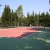 Campo da tennis all'aperto con giocatori. Alberi sullo sfondo.