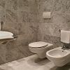 Un bagno con pareti e pavimento in marmo, lavabo, WC, bidet e portasciugamani bianco.