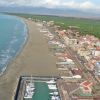 Vista aerea di una spiaggia ampia con edifici e un piccolo porto turistico lungo la costa.