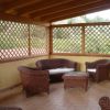 Veranda con mobili in vimini su pavimento in mattonelle, circondata da grigliati di legno.